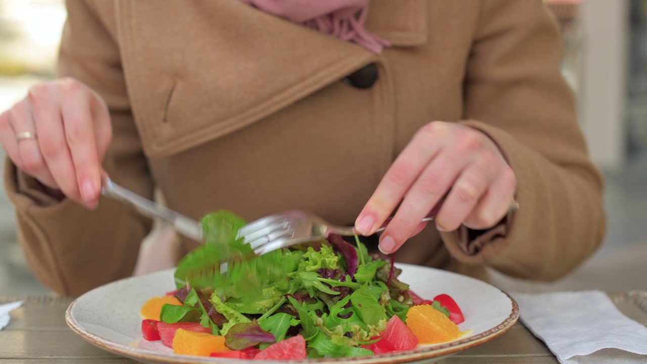 Woman in brown coat eating a salad at a terrace