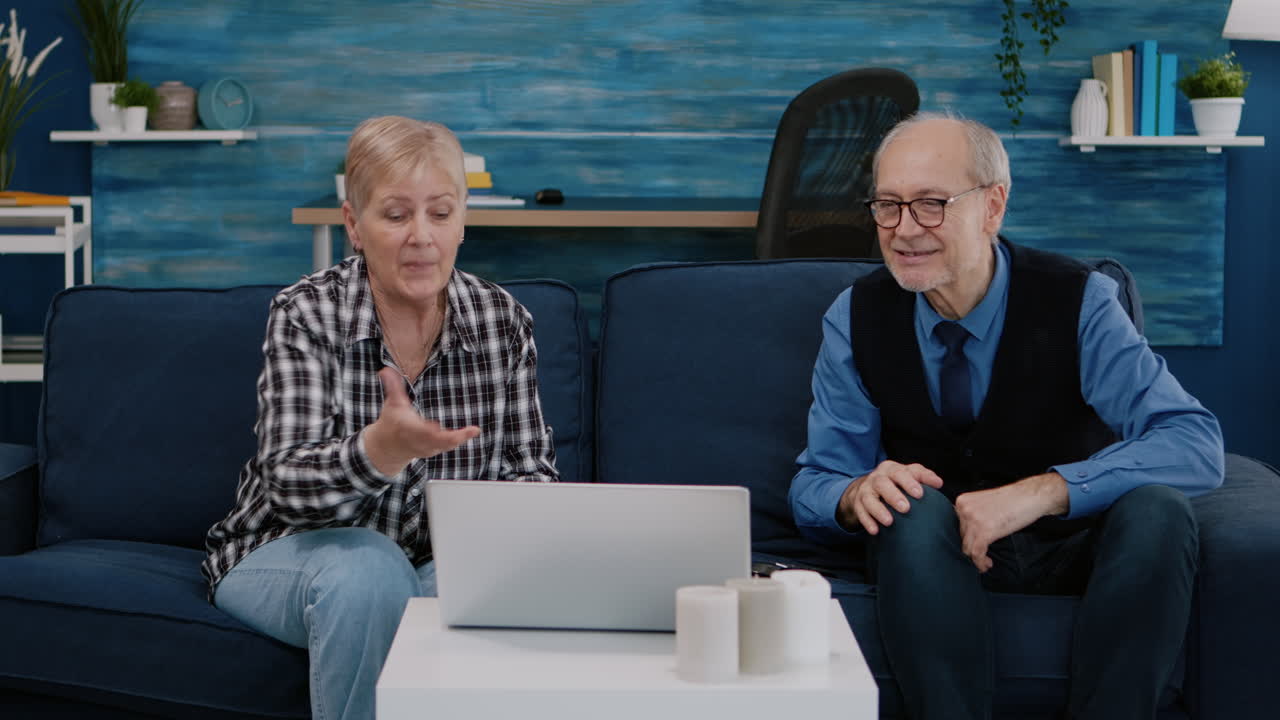 Smiling senior couple looking at laptop computer waving during videocall