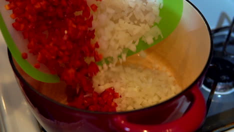 dumping chopped red bell peppers and onions into a pot to saute