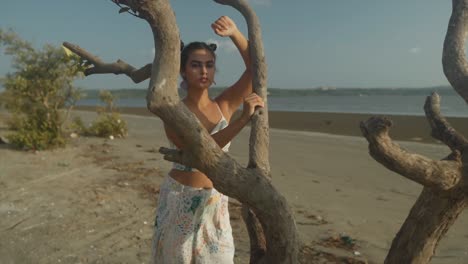 fashionable-emancipated-young-adult-female-hipster-gen-z-teen-girl-serious-face-with-knot-hair-and-nose-piercing-wearing-earrings-looking-at-camera-posing-on-the-beach,-sunny-head-body-shot-portrait