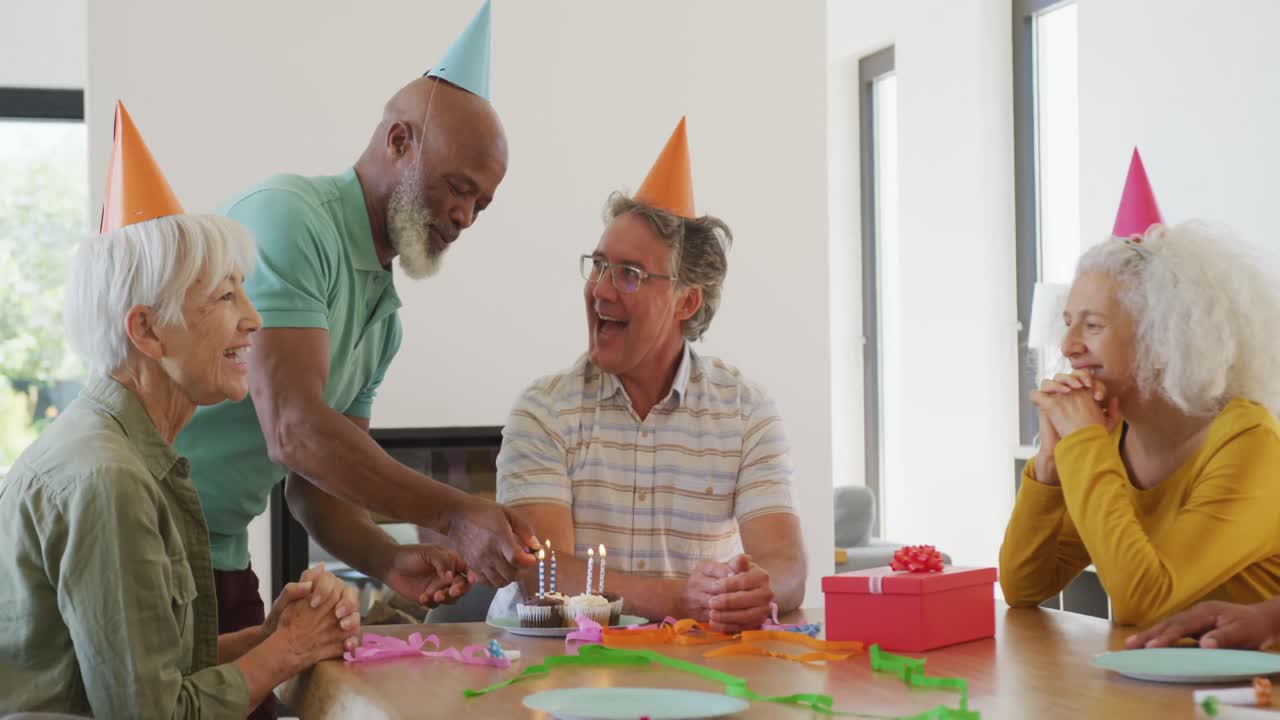 Anziani felici e diversi a una festa di compleanno con torta in una casa di riposo.
