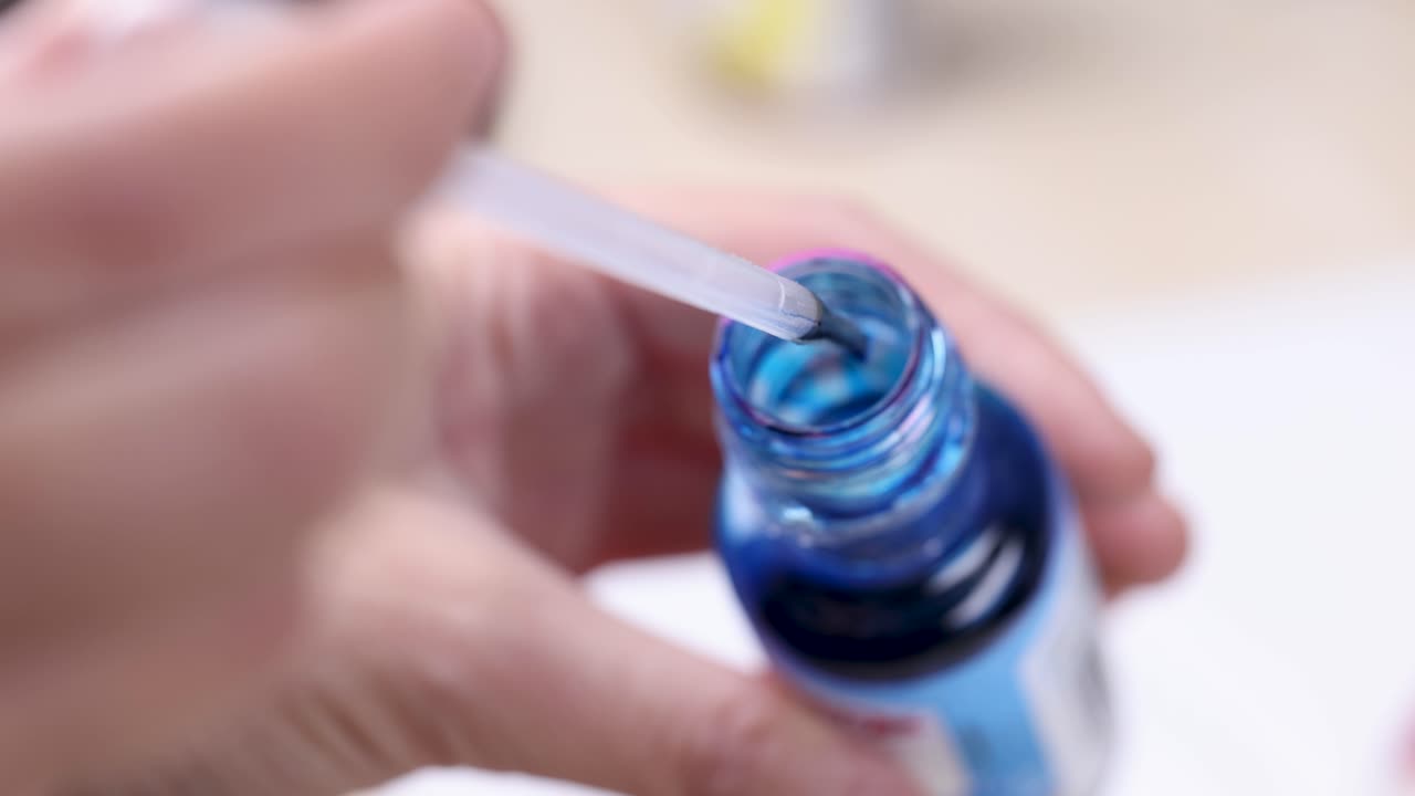 Hand extracts blue liquid from bottle with dropper in bright, close-up kitchen or lab setting