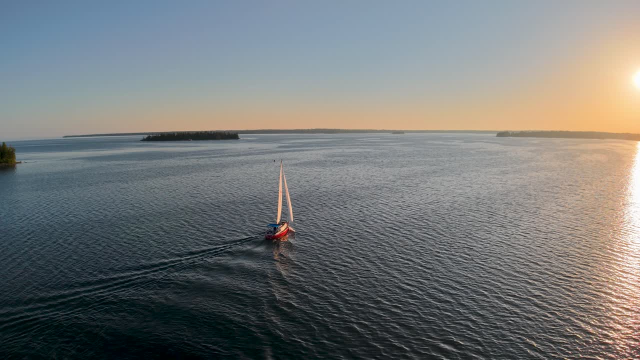 Aerial drone video of a sailboat gliding across calm waters at sunset in the Les Cheneaux Islands of Michigan’s Upper Peninsula