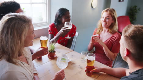 elevated view of five young adult friends sitting with drinks at a table in a pub talking, selective focus