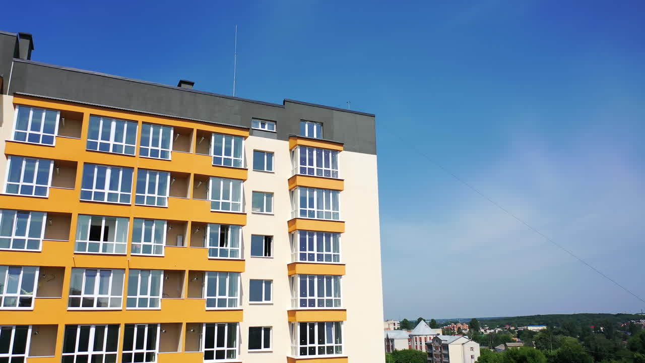 New multi-storey building in the city. Contemporary apartment building with large windows and colorful walls of the facade of a new house for city residents on sky background.