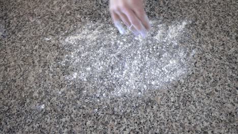 esparciendo harina de pan sobre una encimera de granito mientras se prepara para amasar y cocinar bagels caseros de lechuga