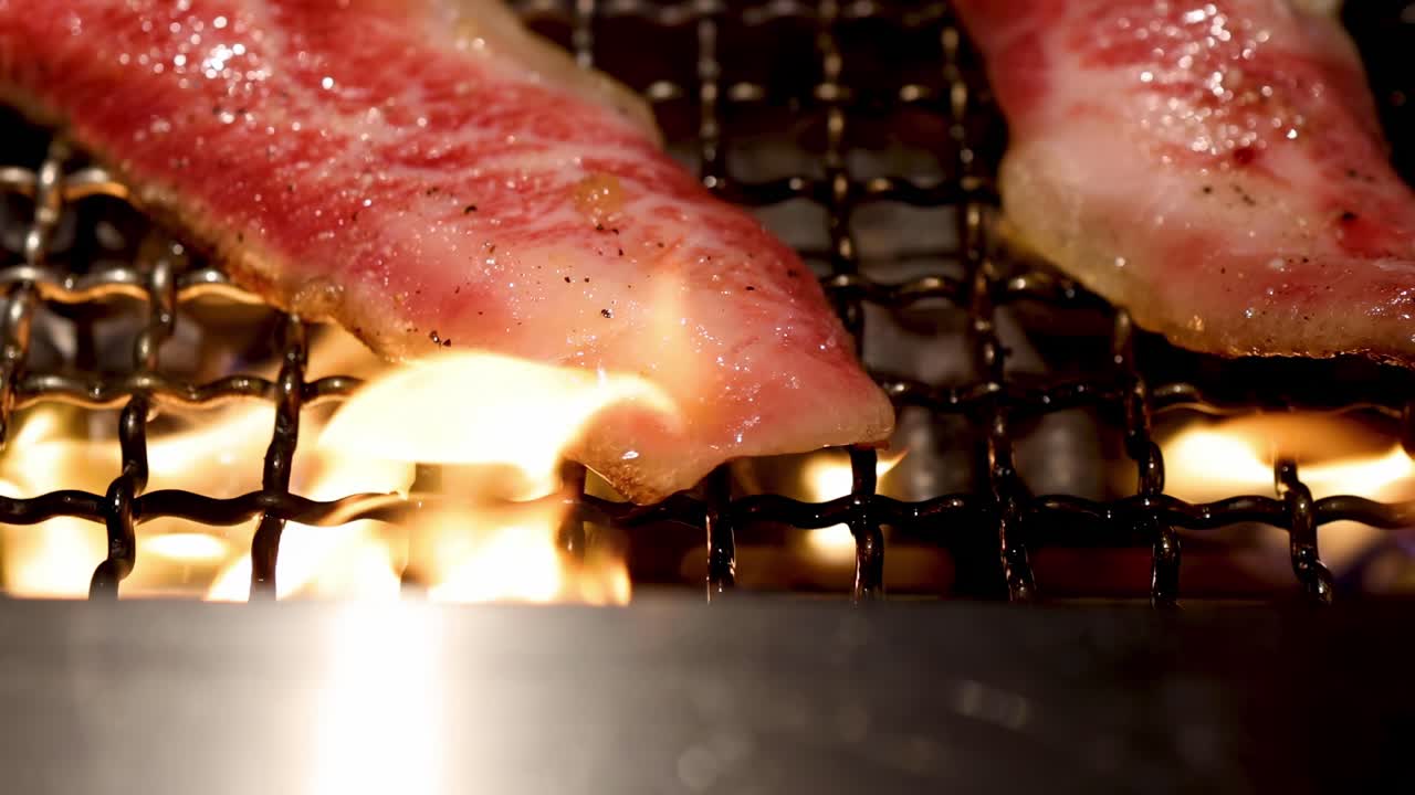 Close-up of beef strips sizzling on a grill with visible flames underneath, highlighting the cooking process.