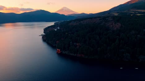 the tranquil shrine sits on the shores of lake ashi, framed by the warm golden hues of the setting sun in japan.