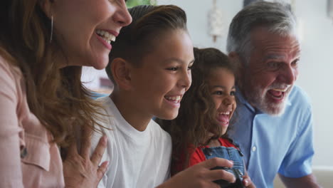 abuelos hispanos con nietos jugando videojuegos en casa sentados en el sofá juntos