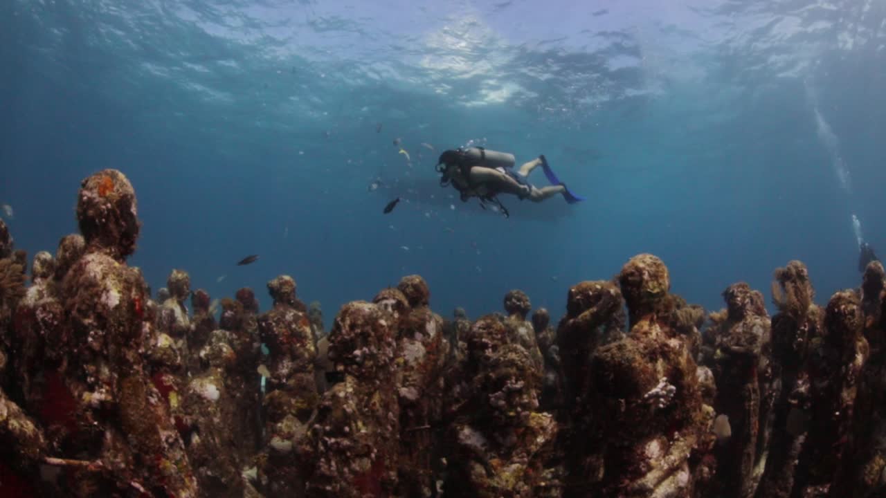 Diver swimming across underwater museum, MUSA artificial reef sculptures. Isla Mujeres, Mexico.