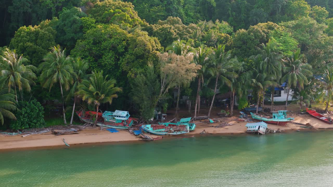 Drone orbit revealing abandoned fishing vessels stranded on tropical beach lined with palm trees and dense jungle