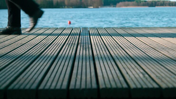 A Man Walking On A Wooden Walkway Near The Lake Shore - Medium Shot