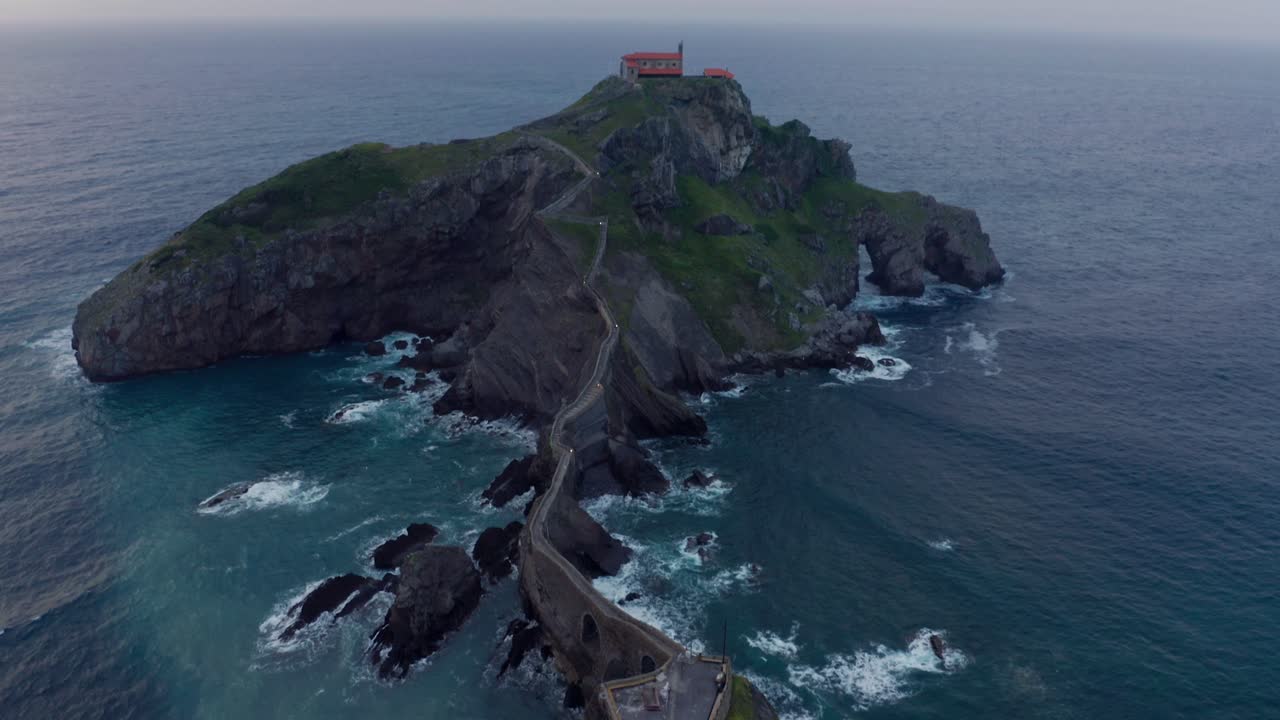 Oceano increspato vicino a una montagna verde con un sentiero sotto il cielo