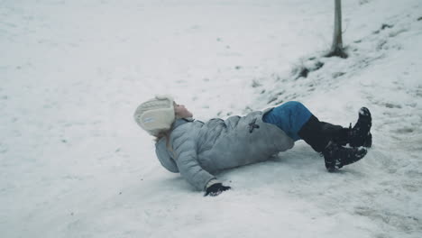 niña rueda por una colina nevada después de luchar para deslizarse hacia atrás, cámara lenta