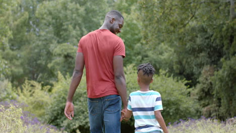 african american father and son walk hand in hand in a lush park at home