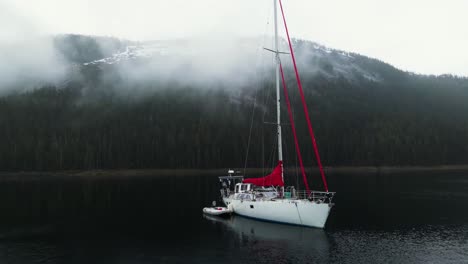 Drone-shot-orbiting-a-sailboat-anchored-in-middle-of-foggy-mountains-of-Alaska