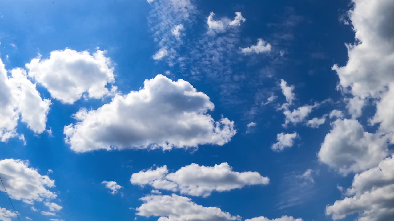 Little fluffy white clouds move by the azure sky. Low angle view at the beautiful clouds lit with bright summer sky. Timelapse.