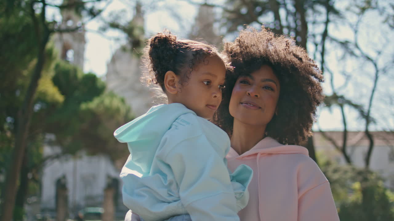 mujer sonriente llevando a un niño a pasear en un parque soleado de cerca. niña relajándose con su madre
