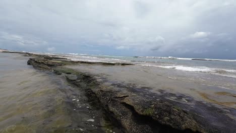 Beautiful-slow-motion-landscape-shot-of-the-calm-Tibau-do-Sul-beach-with-large-rocks-blocking-the-waves-near-Pipa,-Brazil-in-Rio-Grande-do-Norte-during-a-cloudy-summer-day