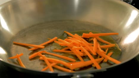 cooking asian food with fresh carrots in a steel pan, handheld close up shot