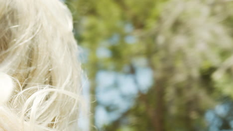 blonde woman rides in a car with the wind in her hair and trees and palm trees in the background