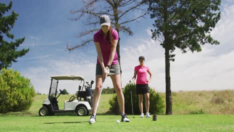 Two-caucasian-women-playing-golf-one-taking-shot-from-bunker