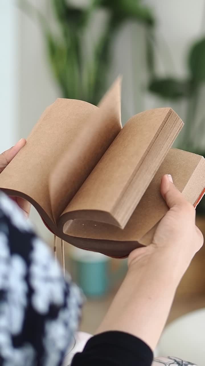 Primo piano di mani che sfogliano pagine vuote di un quaderno di carta kraft