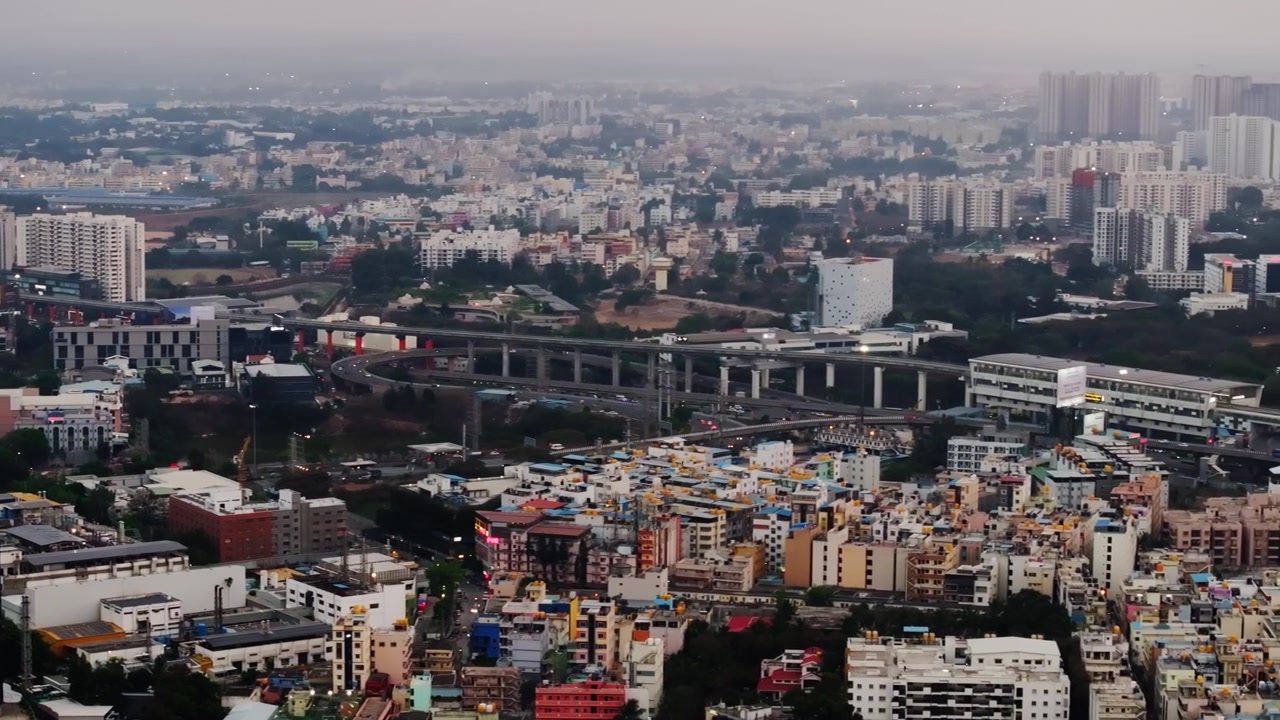 Edifici residenziali con appartamenti a torre, cavalcavia, linea della metropolitana, foschia e la stazione della metropolitana Infosys a Electronic City, Bengaluru, Karnataka, India. Di giorno, panoramica, ripresa con drone, 4K.
