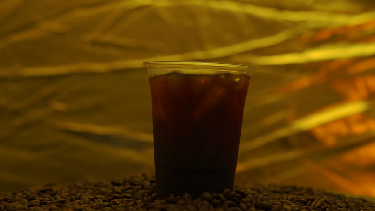 Black Coffee Iced In Disposable Plastic Cup On Roasted Coffee Bean Rotated.