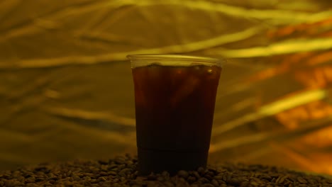 black coffee iced in disposable plastic cup on roasted coffee bean rotated.