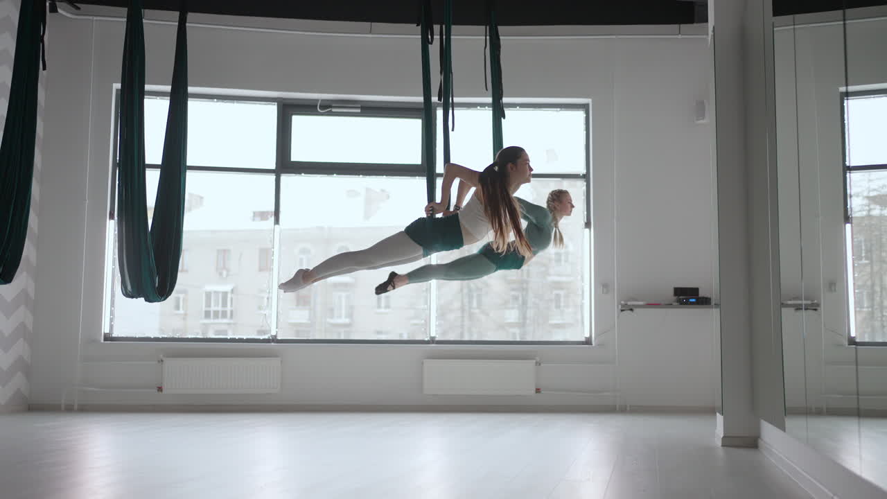 dos jóvenes mujeres yogi practicando yoga aéreo en hamacas verdes en un club de fitness. hermosas mujeres trabajando en clase realizando aero yoga. variación de la postura de la pirámide parsvottanasana