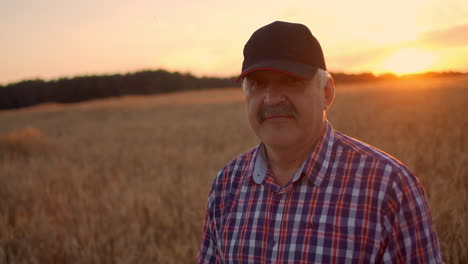 Retrato-De-Un-Feliz-Granjero-Adulto-Mayor-Con-Una-Gorra-En-Un-Campo-De-Grano-Mirando-La-Puesta-De-Sol.-Campo-De-Trigo-De-Cereales-Al-Atardecer.-Camara-Lenta