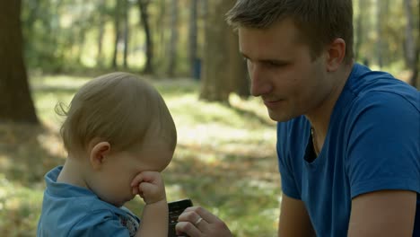 father helps crying son to use cell phone in park