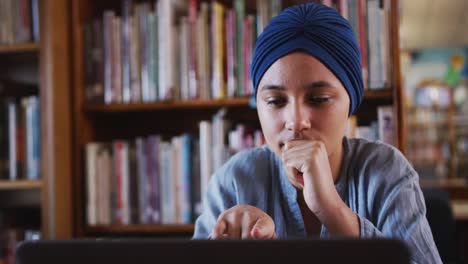 Asiatische-Studentin,-Die-Einen-Blauen-Hijab-Trägt,-Sitzt-Und-Benutzt-Einen-Laptop-In-Der-Bibliothek