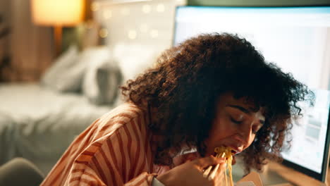 woman eating takeout noodles in bedroom