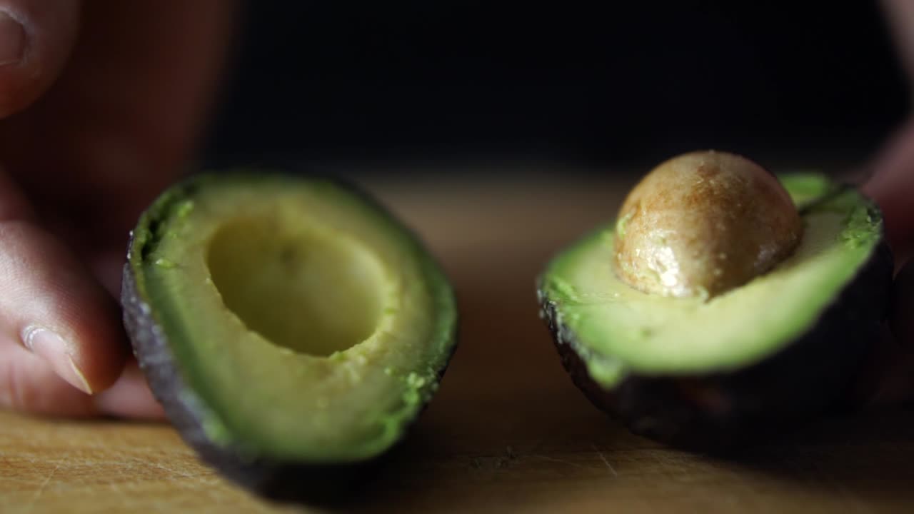mani del maschio caucasico apertura avocado verde tagliato a metà sul tagliere di legno, rallentatore