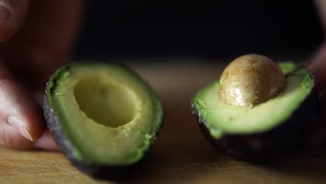 hands of caucasian male opening green avocado cut in half on wooden chopping board, slow motion