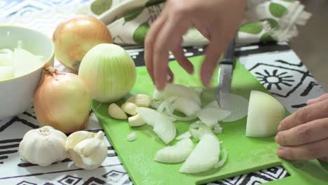 Brunette woman's hands cutting onion slices, on a green cutting board, on a kitchen table. Preparing a salad.
