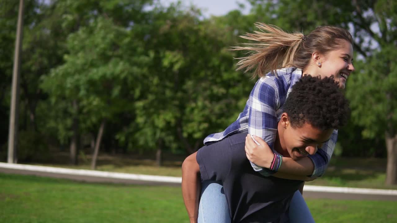 Romantic date of a happy multi ethnic couple: handsome african guy piggybacking his caucasian happy girlfriend and spinning her
