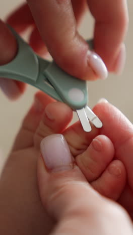 caring about the child. mom's hands hold the tiny toes and cut the toenails with scissors. close up. blurred backdrop. vertical video