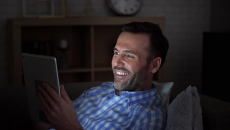 Man-lying-on-the-sofa-and-using-tablet-at-night