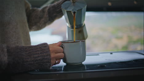 lady hands filling coffee cup from moka pot at trailer close up. woman pouring