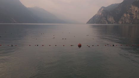 Ein-Einsamer-Mann,-Der-An-Einem-Dunstigen-Sommermorgen-Auf-Dem-Dock-Sitzt-Und-Einen-Atemberaubenden-Blick-Auf-Den-See-Hat