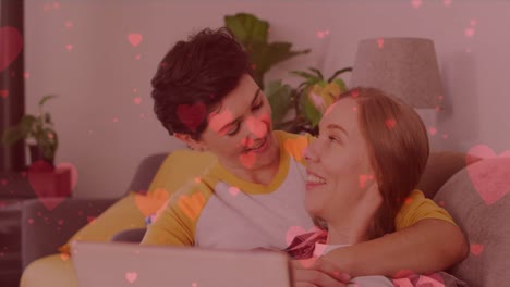 animation of heart emojis over happy caucasian female couple in love embracing