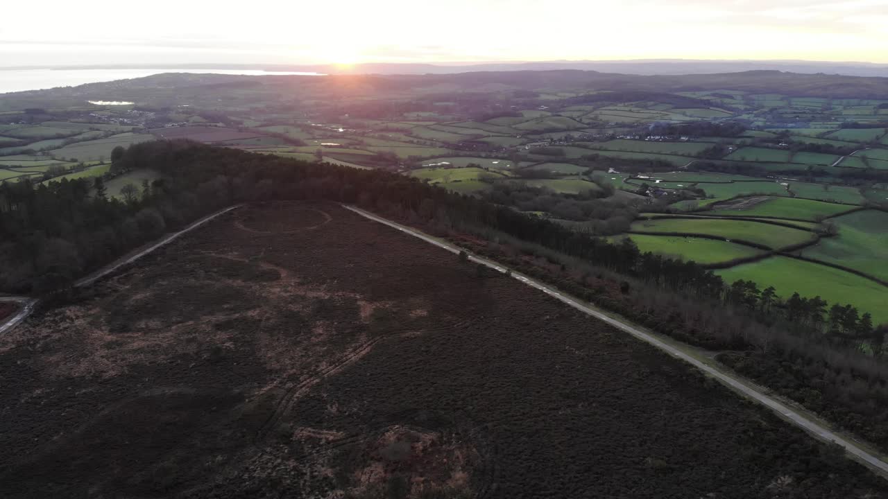 Sunset illuminating Mutters Moor and the surrounding countryside near Sidmouth, East Devon, aerial view at golden hour. rising shot