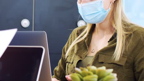 Junge-Frau-Mit-Gesichtsmaske-Tippt-Auf-Laptop-Im-Modernen-Büro