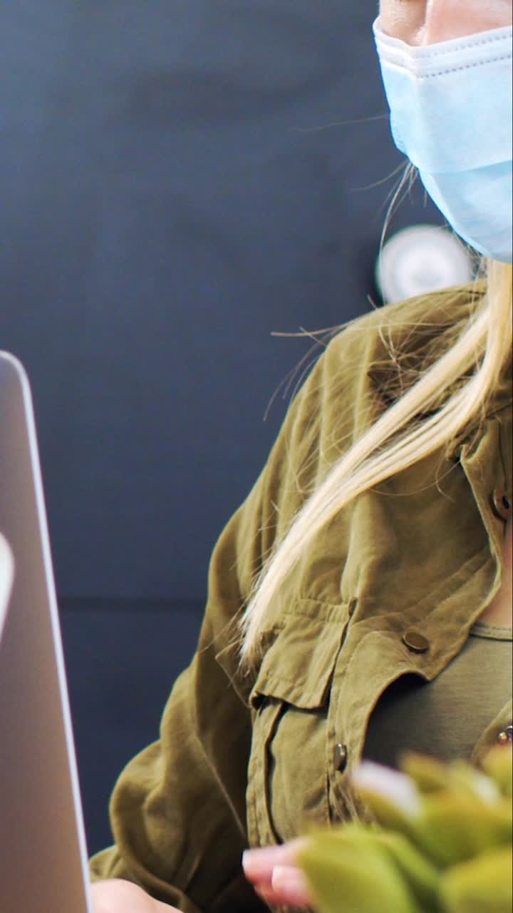 mujer joven con mascarilla escribiendo en una laptop en una oficina moderna