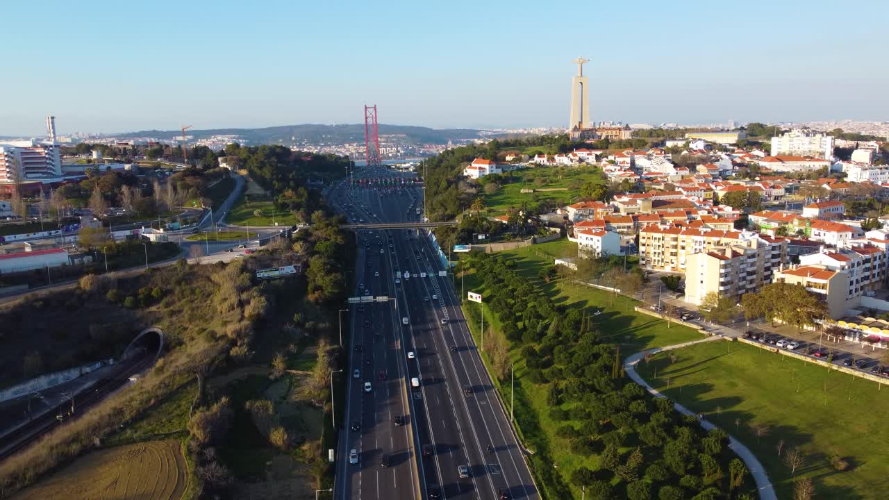 Drone Parallax shot to the left over a highway facing towards the 25th of April bridge in Lisbon with Cristo Rei in the Background