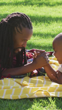 video of happy african american father and son having picnic on grass, arm wrestling