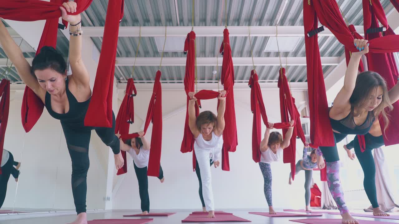 le donne stanno su una gamba tenendo una amaca da yoga volante sopra la testa